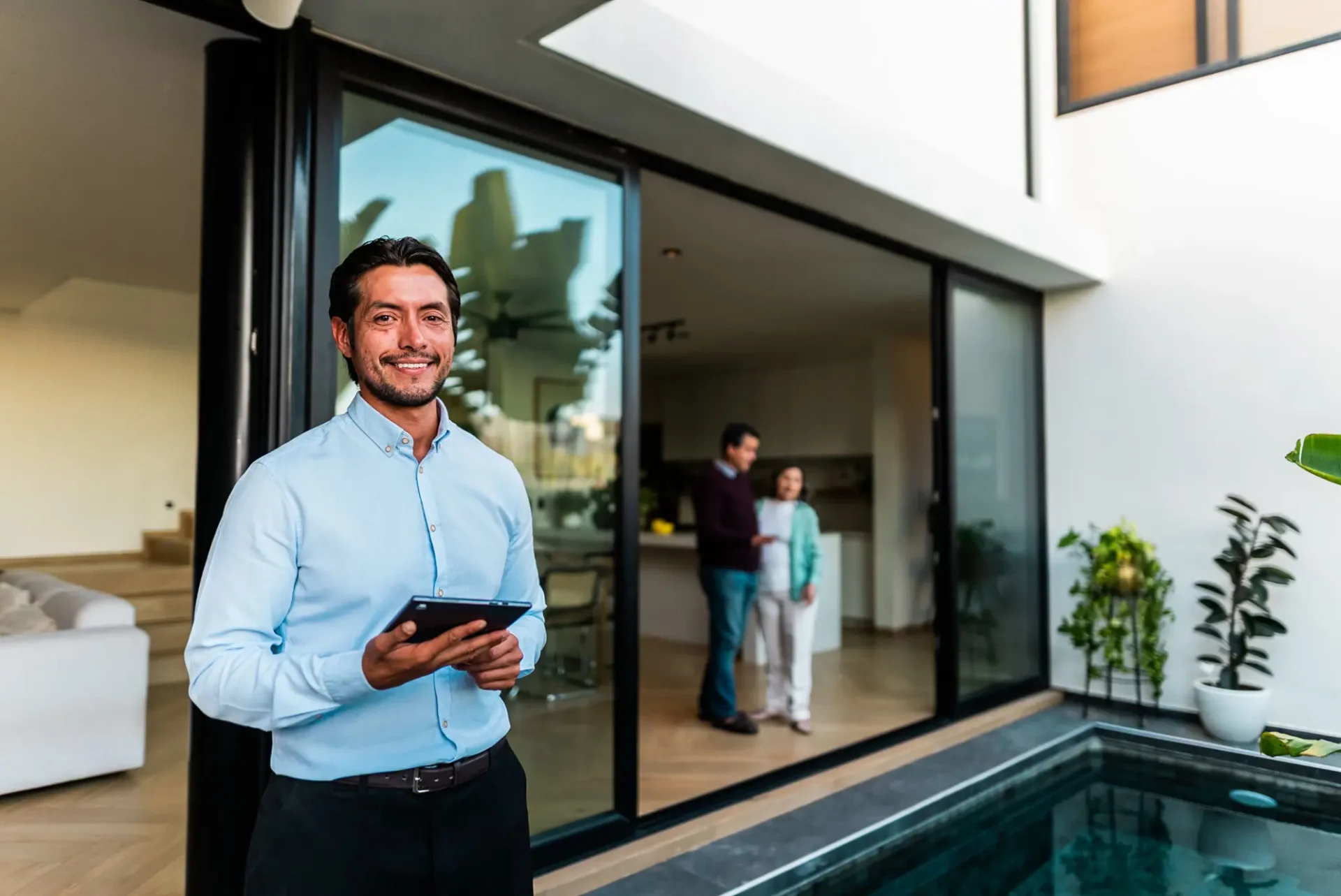 Man smiling outside modern house with tablet.