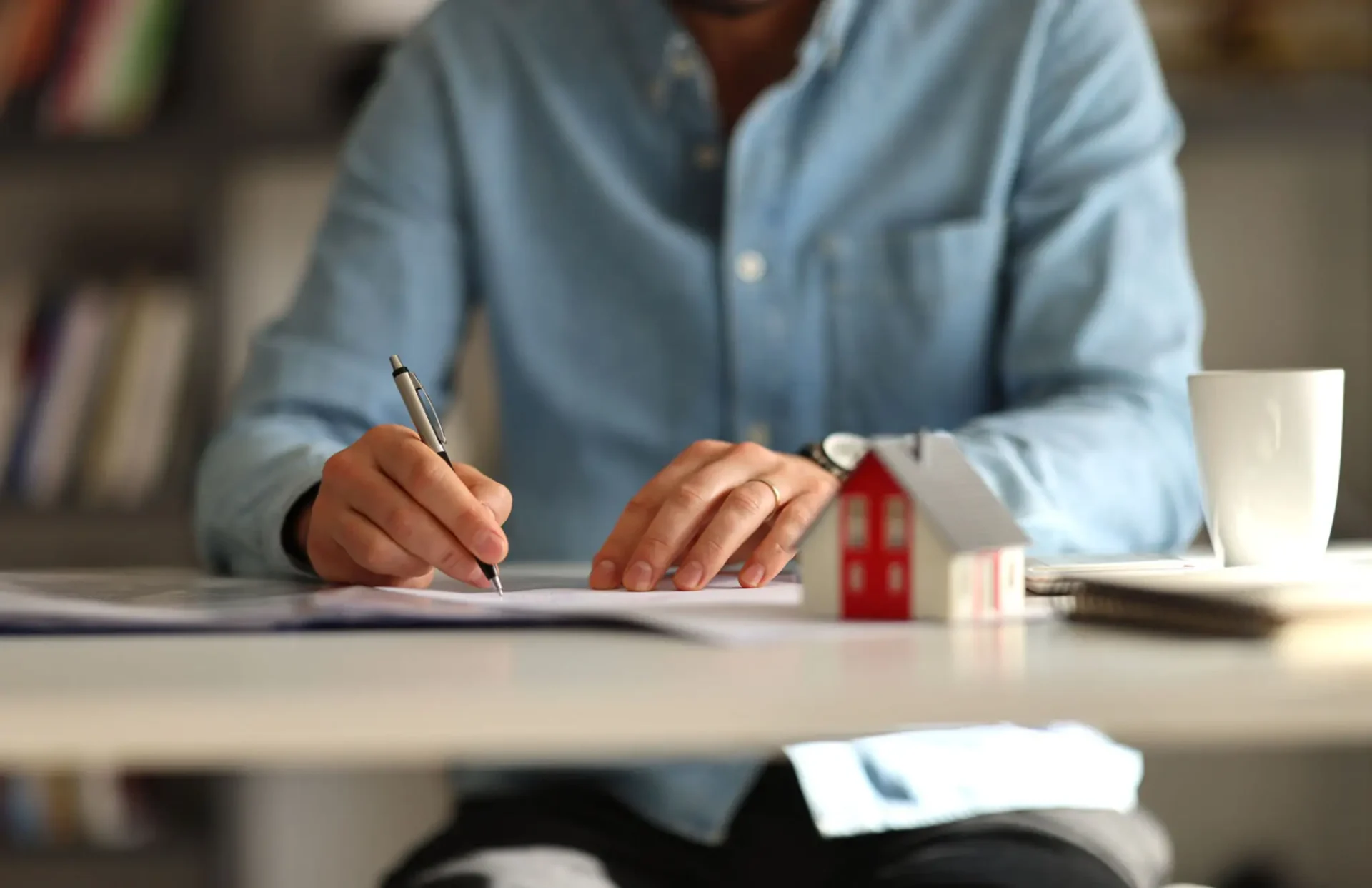 Man writing at desk with paper house.