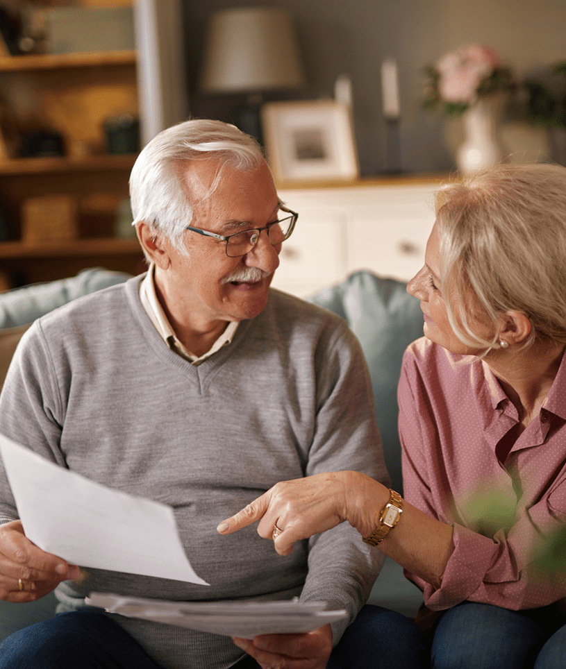 Elderly couple discussing documents on couch.